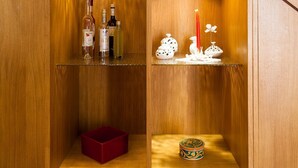 Uma escada de madeira com prateleiras embutidas, exibindo garrafas, uma caixa vermelha e objetos decorativos.