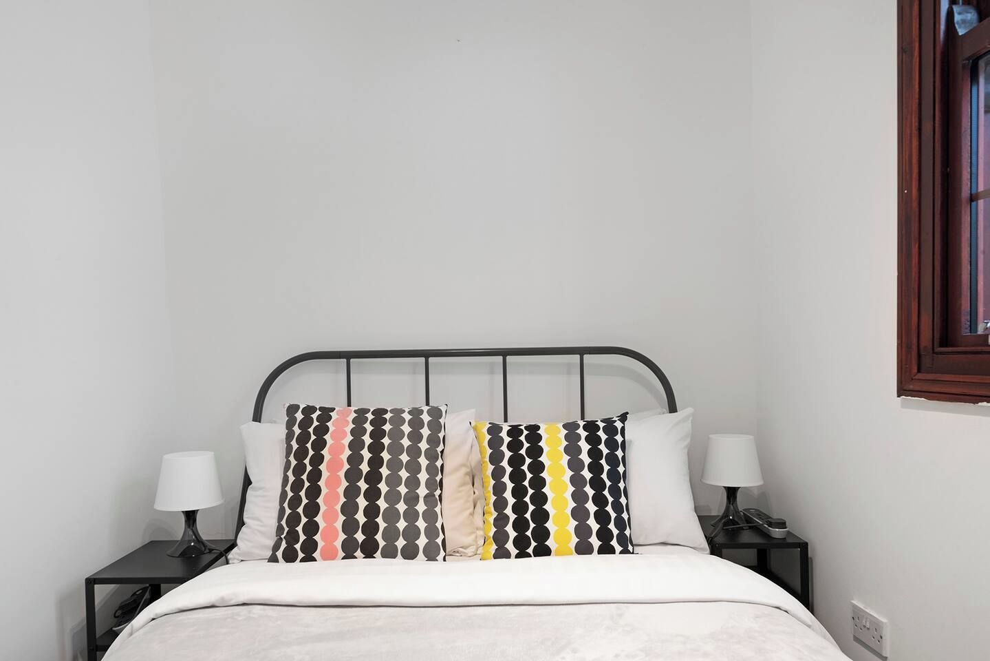 A bed with a metal frame, two bedside tables with lamps, and a window with a wooden frame.