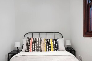 Ein Bett mit Metallgestell, zwei Nachttische mit Lampen und ein Fenster mit Holzrahmen.