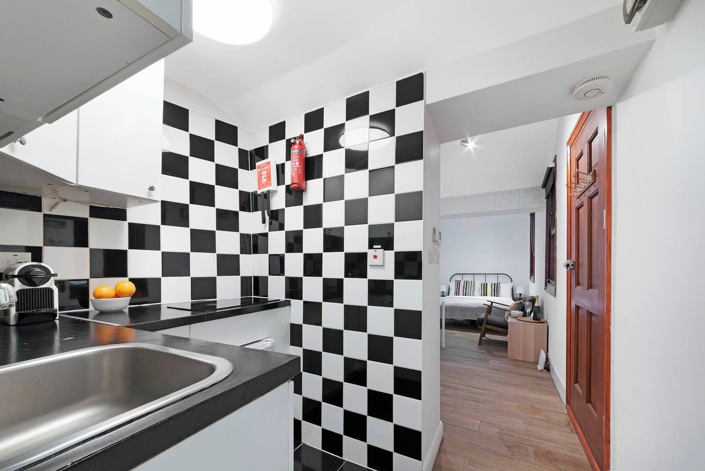 Een moderne keuken met zwart-wit geruite tegels, een roestvrijstalen spoelbak en een rode brandblusser.