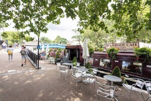 An outdoor cafe with tables and chairs, a sign for 'Waterside Cafe', and a pathway with people walking.