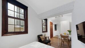 Een slaapkamer met een groot raam, een eethoek met een tafel en stoelen, en een aan de muur bevestigde televisie.
