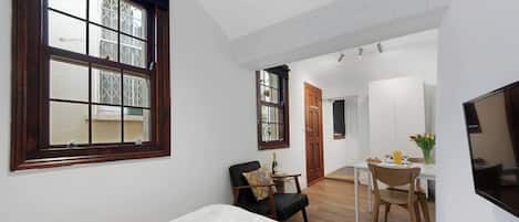 Une chambre avec une grande fenêtre, un coin repas avec une table et des chaises, et un téléviseur fixé au mur.