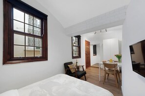 A bedroom with a large window, a dining area with a table and chairs, and a TV mounted on the wall.