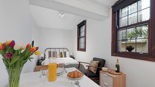 Hotelkamer met een bed, een ontbijt gedekte eettafel, een vaas tulpen en een raam met uitzicht op groen.