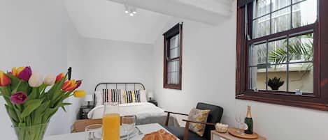 Hotelkamer met een bed, een ontbijt gedekte eettafel, een vaas tulpen en een raam met uitzicht op groen.