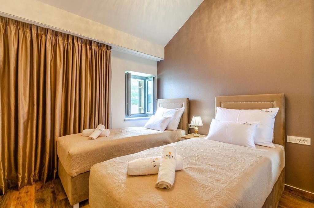 Une chambre d’hôtel avec deux lits, une literie de couleur beige, une fenêtre avec des rideaux et une lampe sur la table de chevet.