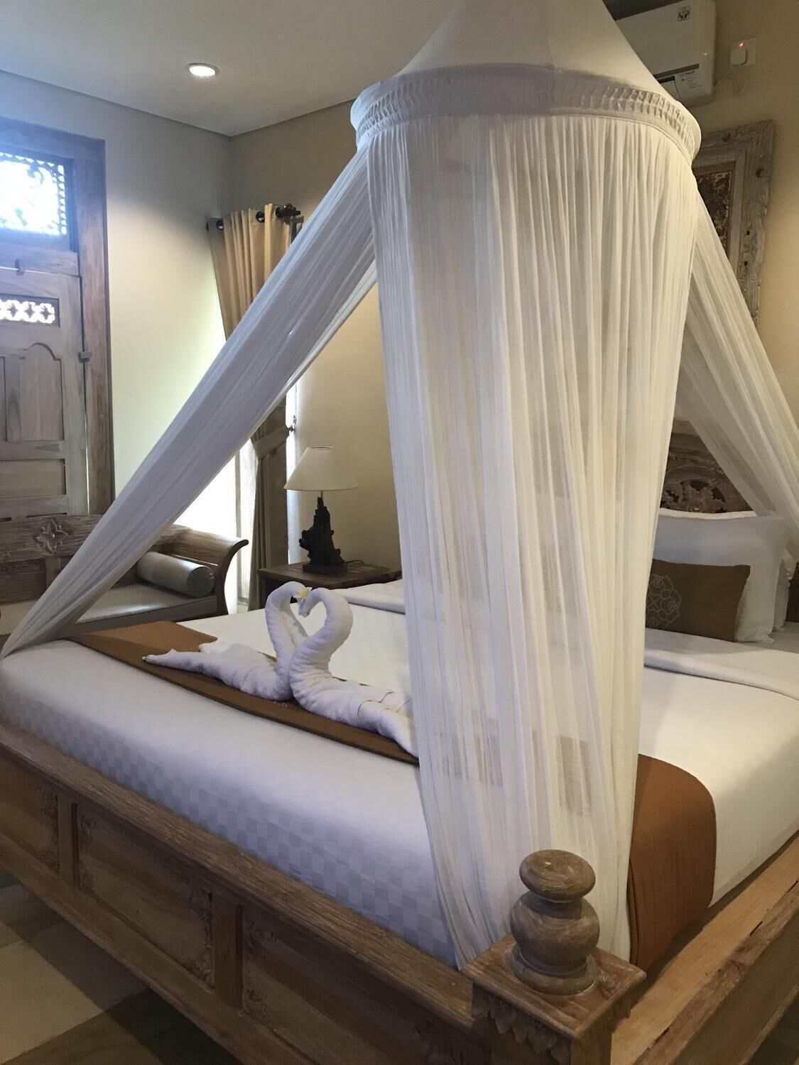Een hemelbed met houten hoofdeinde, een nachtkastje en een decoratieve zwaan als handdoek.
