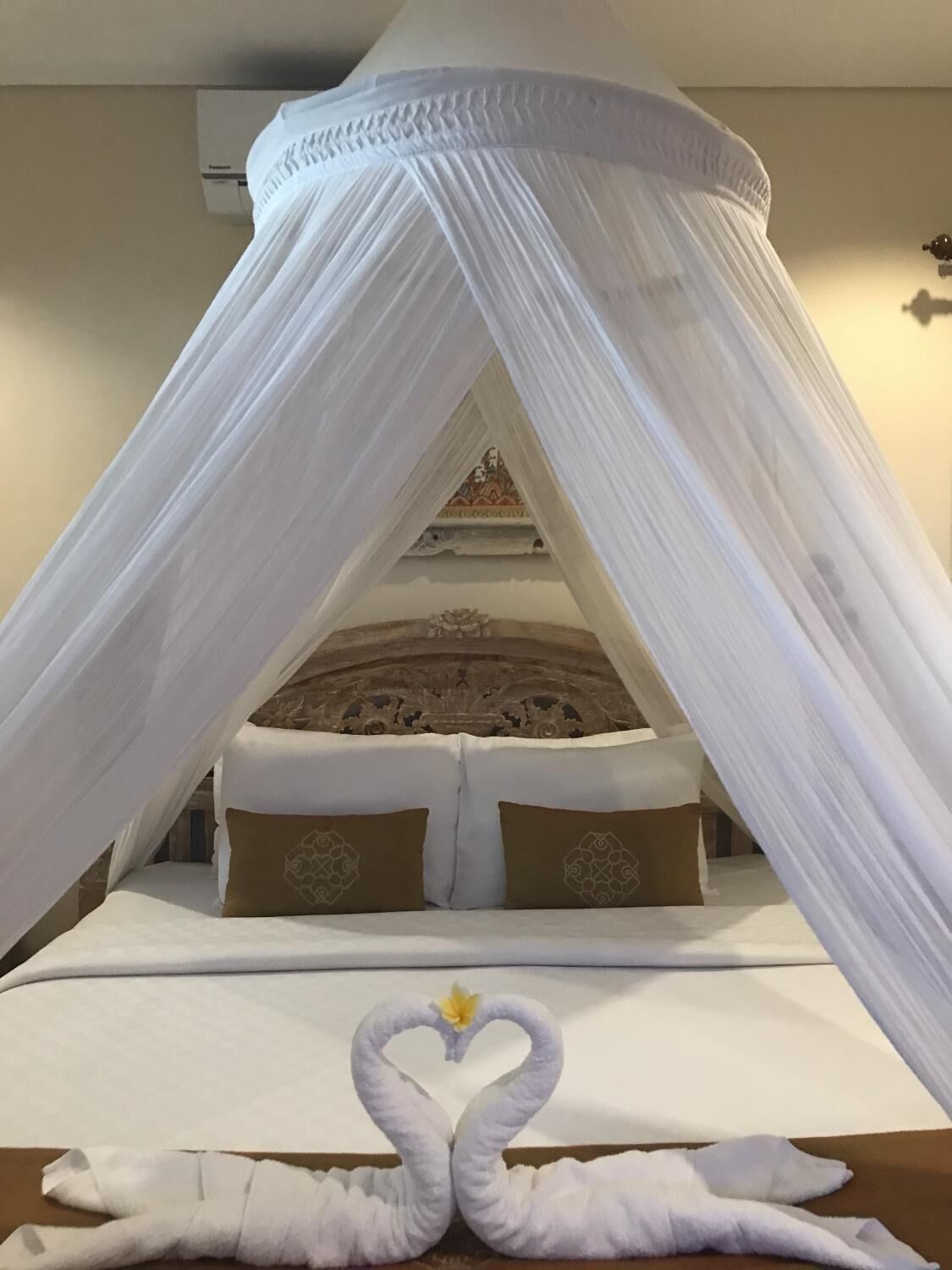 Una cama con dosel, almohadas y dos toallas con forma de cisne.