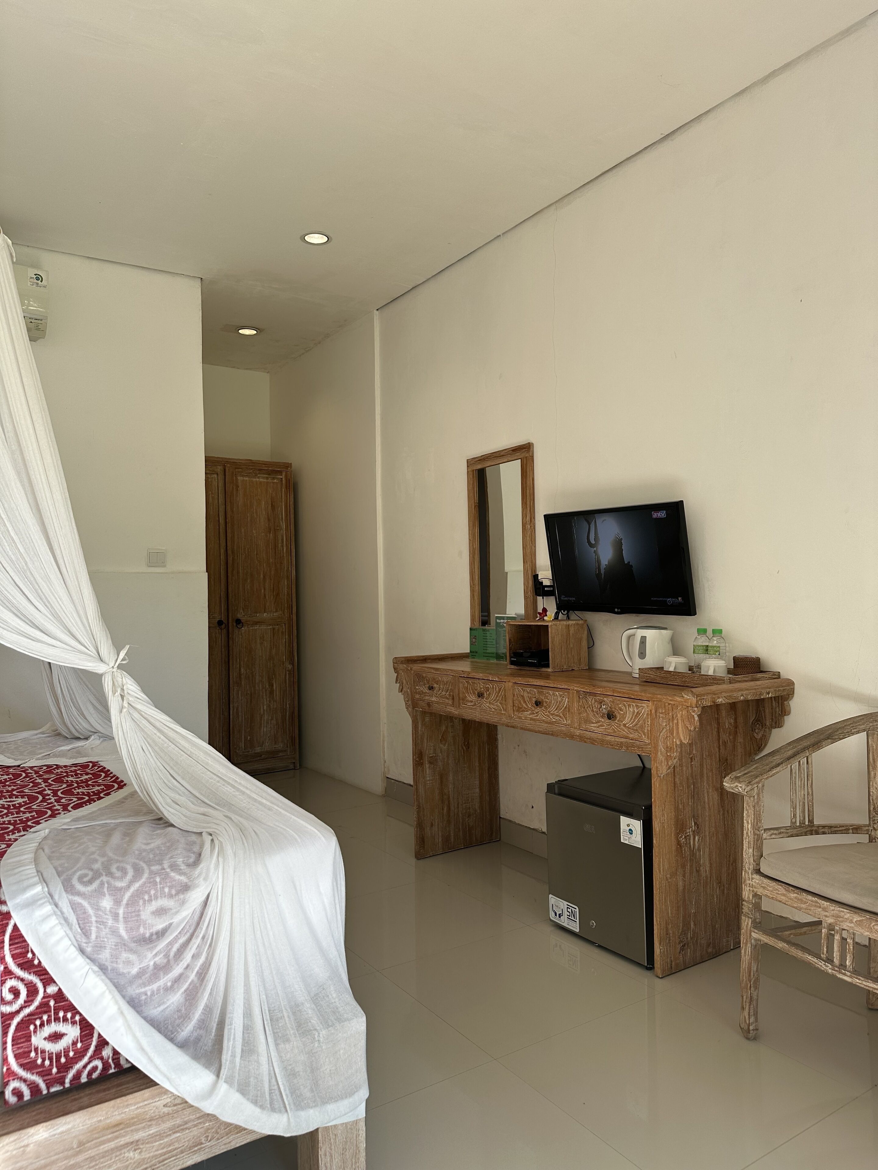 A bedroom with a bed, a wooden desk with a TV, a chair, and a small refrigerator.
