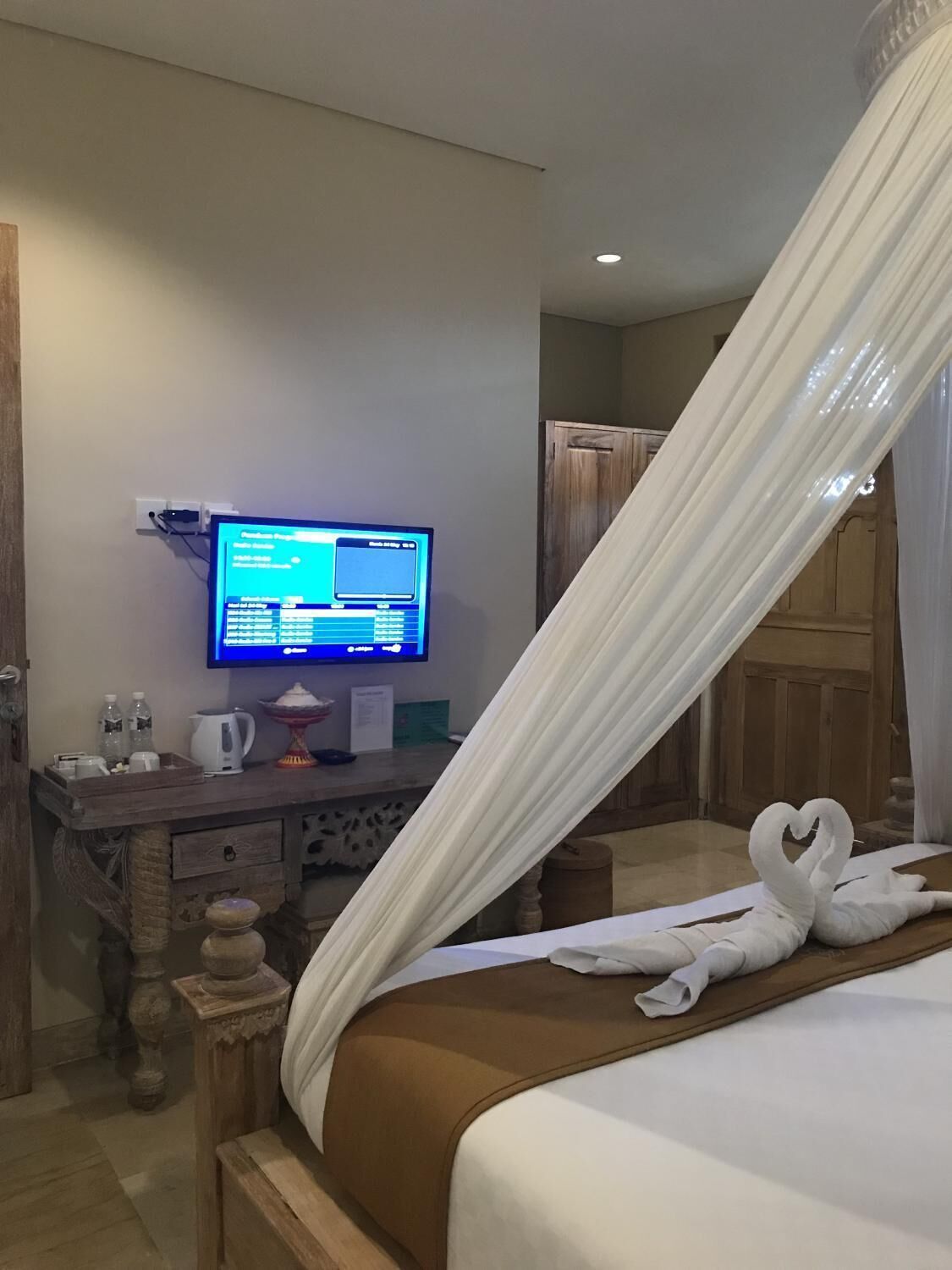 A hotel room with a bed, a television on a wooden dresser, and a canopy over the bed.