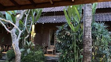 A covered outdoor area with a thatched roof, stone steps leading to a wooden door, and a bench.