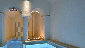 A spacious, well-lit indoor swimming pool with clear water, surrounded by walls with a checkered pattern and a modern architectural design. - The A Collection, Oia by K&K (Santorini)