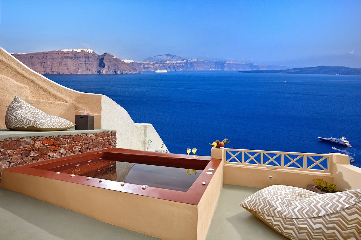 A rooftop terrace with a hot tub, stone wall, and a view of the sea and cliffs.