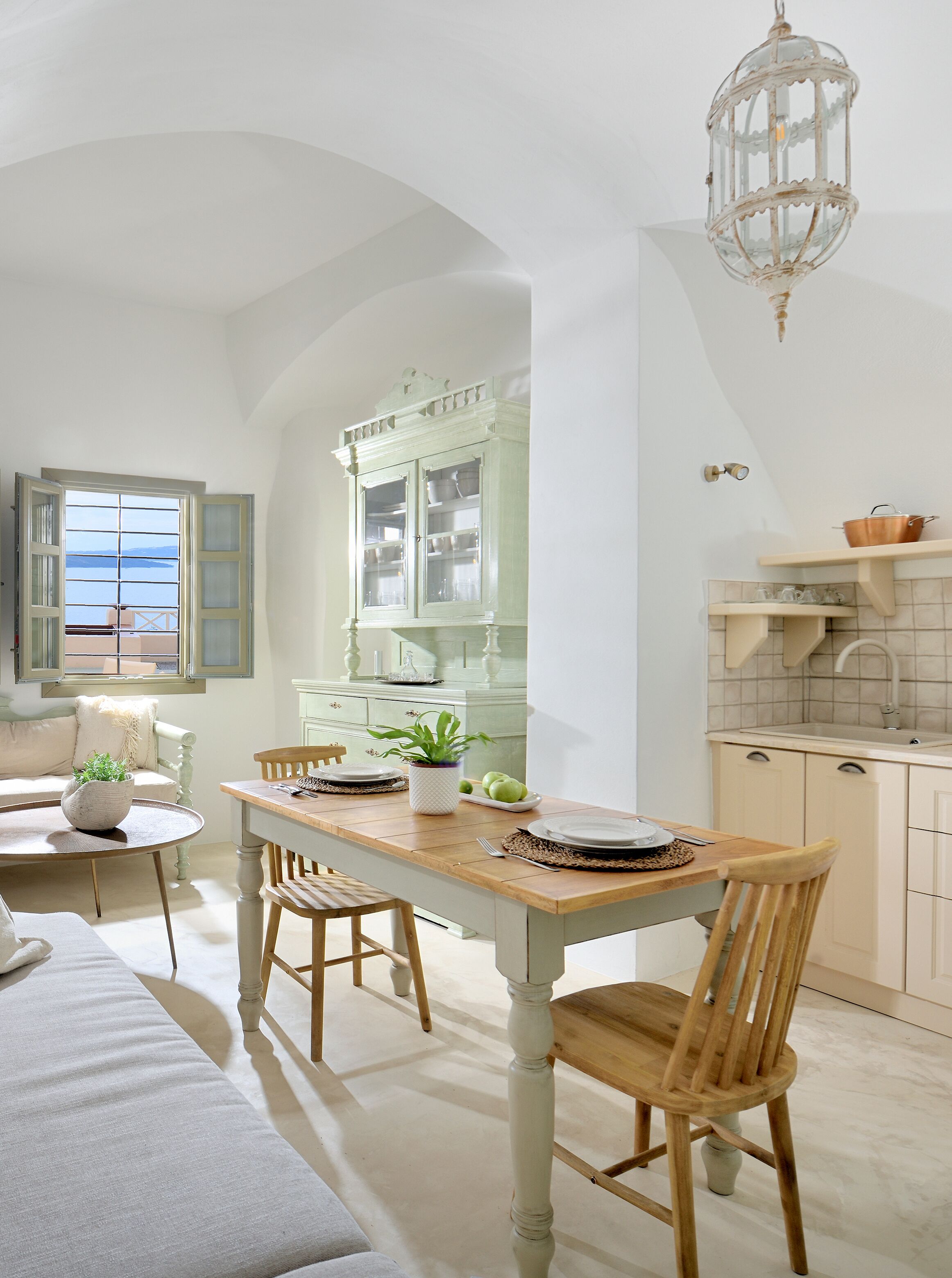 Una cocina luminosa con una mesa y sillas de madera, un armario verde y una lámpara colgante.