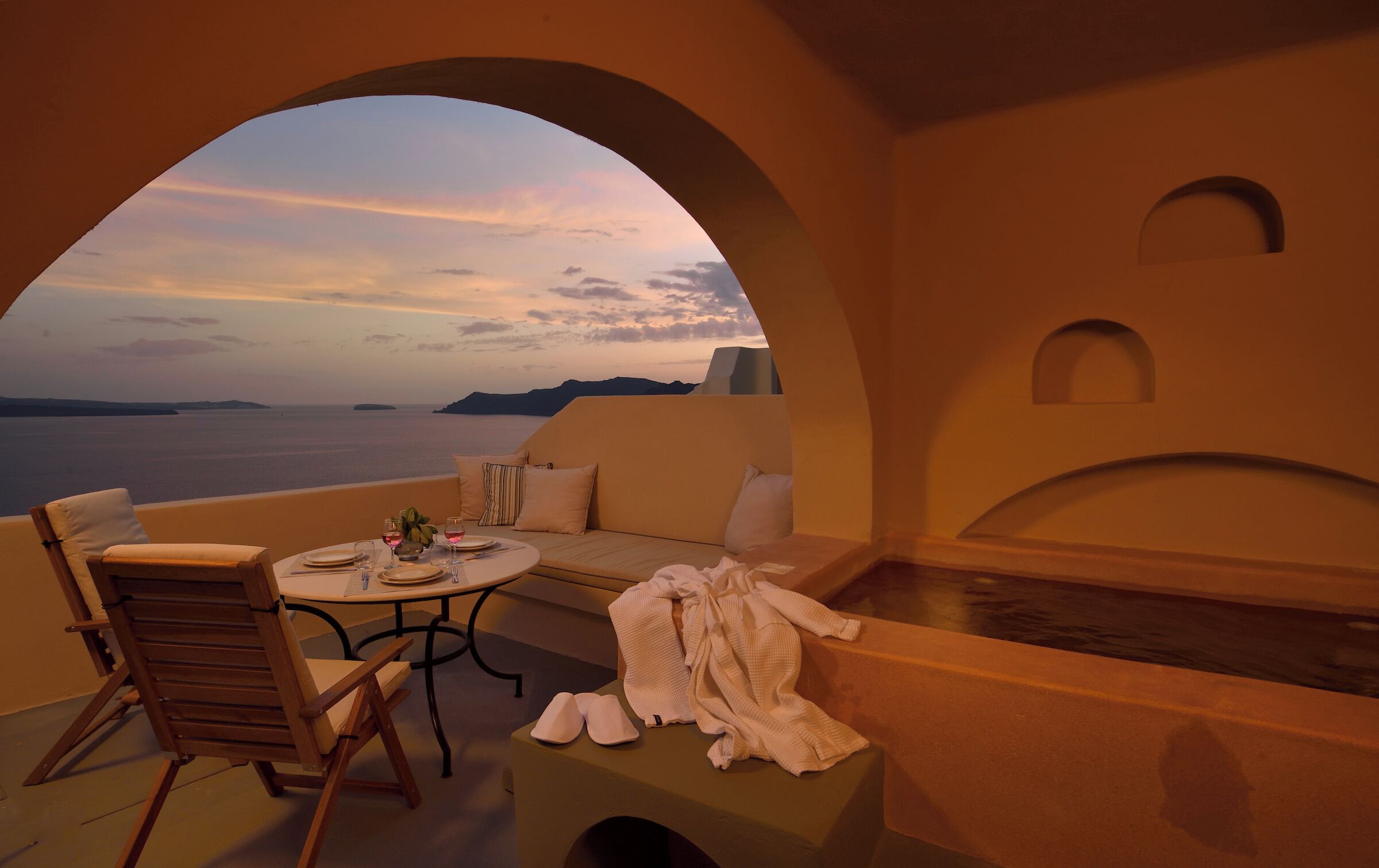 A terrace with a table set for two, a sofa, and a bathtub.
