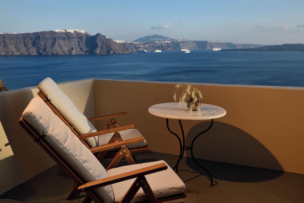 A balcony with two lounge chairs and a small table with a vase of dried plants.