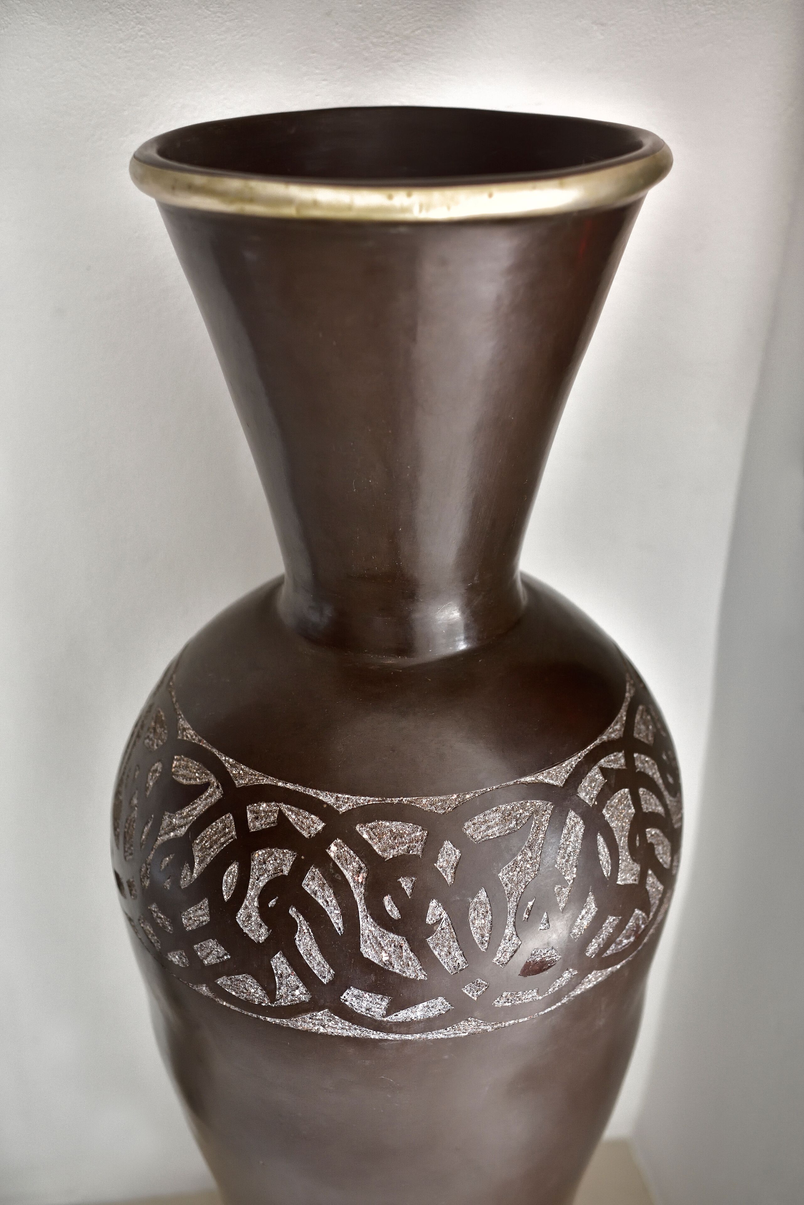 A dark brown vase with a narrow neck and a wider base, featuring intricate silver patterns on its side.