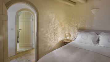 Un dormitorio con una cama, una mesita de noche, una lámpara de pared y un arco que da paso a otra habitación.