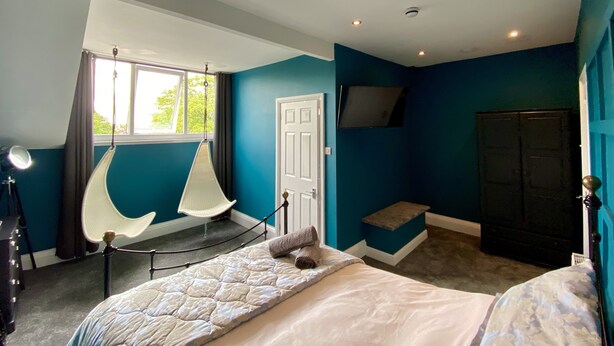 A bedroom with a bed, a hanging chair, a wardrobe, and a door. - Blenheim Guest House York (York)