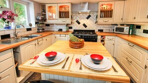 A modern kitchen with white cabinets, a wooden countertop, a central island with a bowl of fruit, and a microwave. - Mallard Cottage (Aylesford)