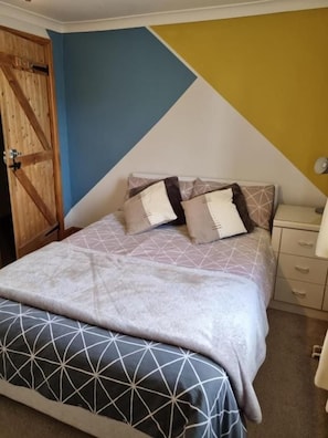 A bedroom with a bed, a nightstand, and a wooden wardrobe. - Mallard Cottage (Aylesford)