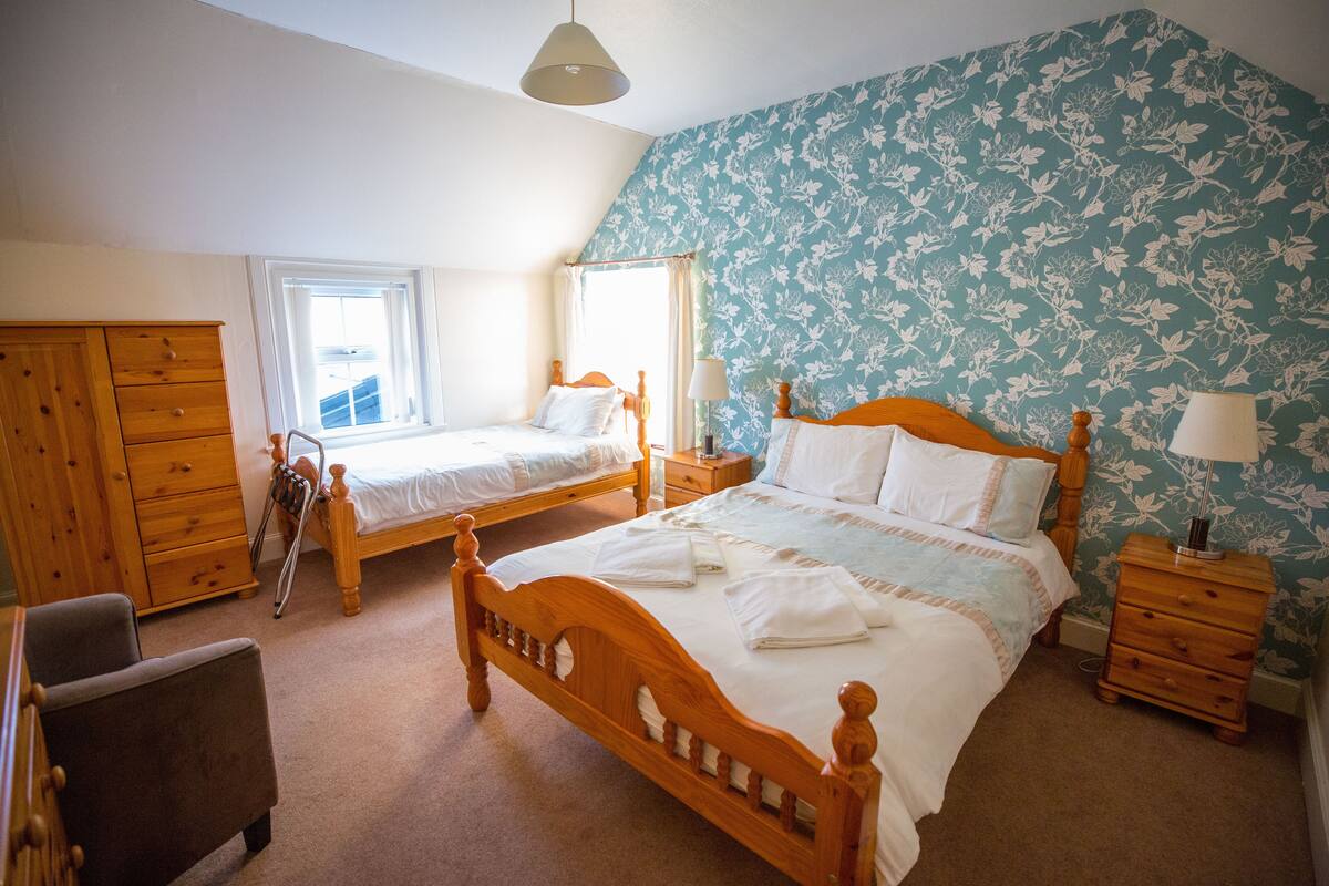 A bedroom with two single beds, a wooden dresser, a chair, and a nightstand with a lamp.