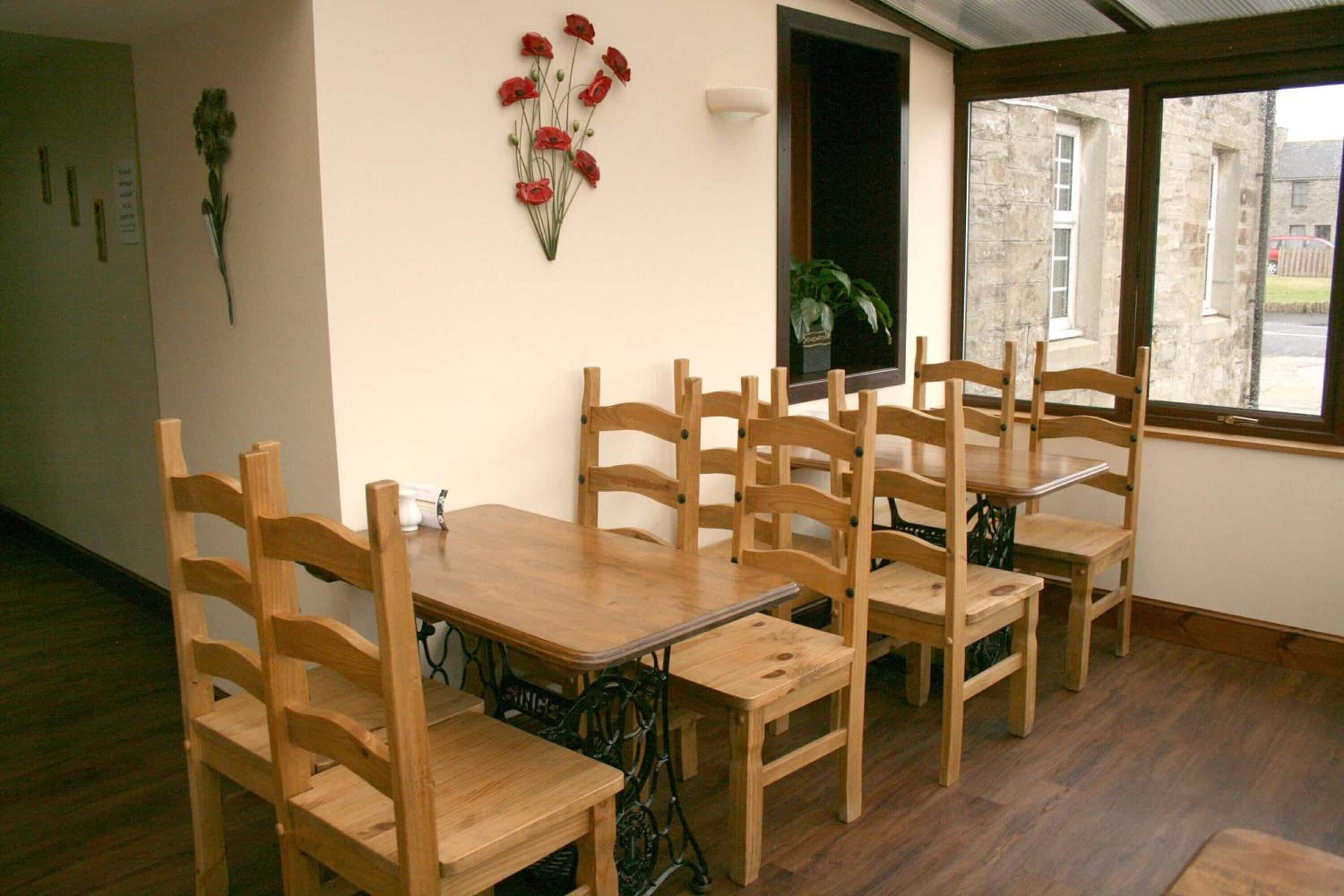 A dining area with wooden tables and chairs, a window with a view of the outside, and a wall-mounted flower decoration.