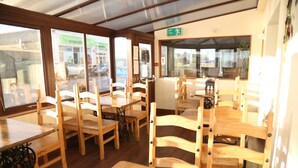 A restaurant interior with wooden tables and chairs, a visible exit sign, and a view of the street outside. - Smithfield guesthouse (Dounby)