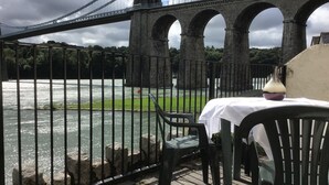 Blick auf einen Fluss mit einer Brücke, einem Tisch mit einer Vase und Stühlen.