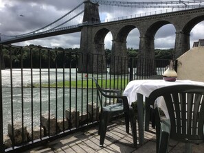 Blick auf einen Fluss mit einer Brücke, einem Tisch mit einer Vase und Stühlen.
