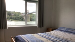 Ein Schlafzimmer mit einem großen Bett, einem Nachttisch aus Holz und einem Fenster mit Vorhängen.