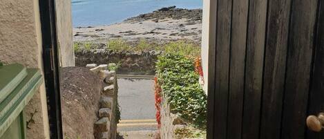 A view through a doorway to a coastal area with a stone staircase leading to a beach.