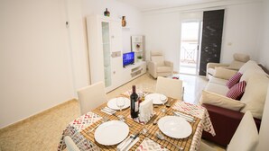 Un comedor con una mesa dispuesta para cuatro personas, un sofá y un televisor al fondo.
