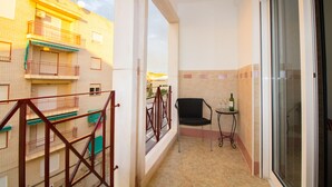 Un balcón con vistas a edificios, una silla, una mesa con una botella y un vaso.