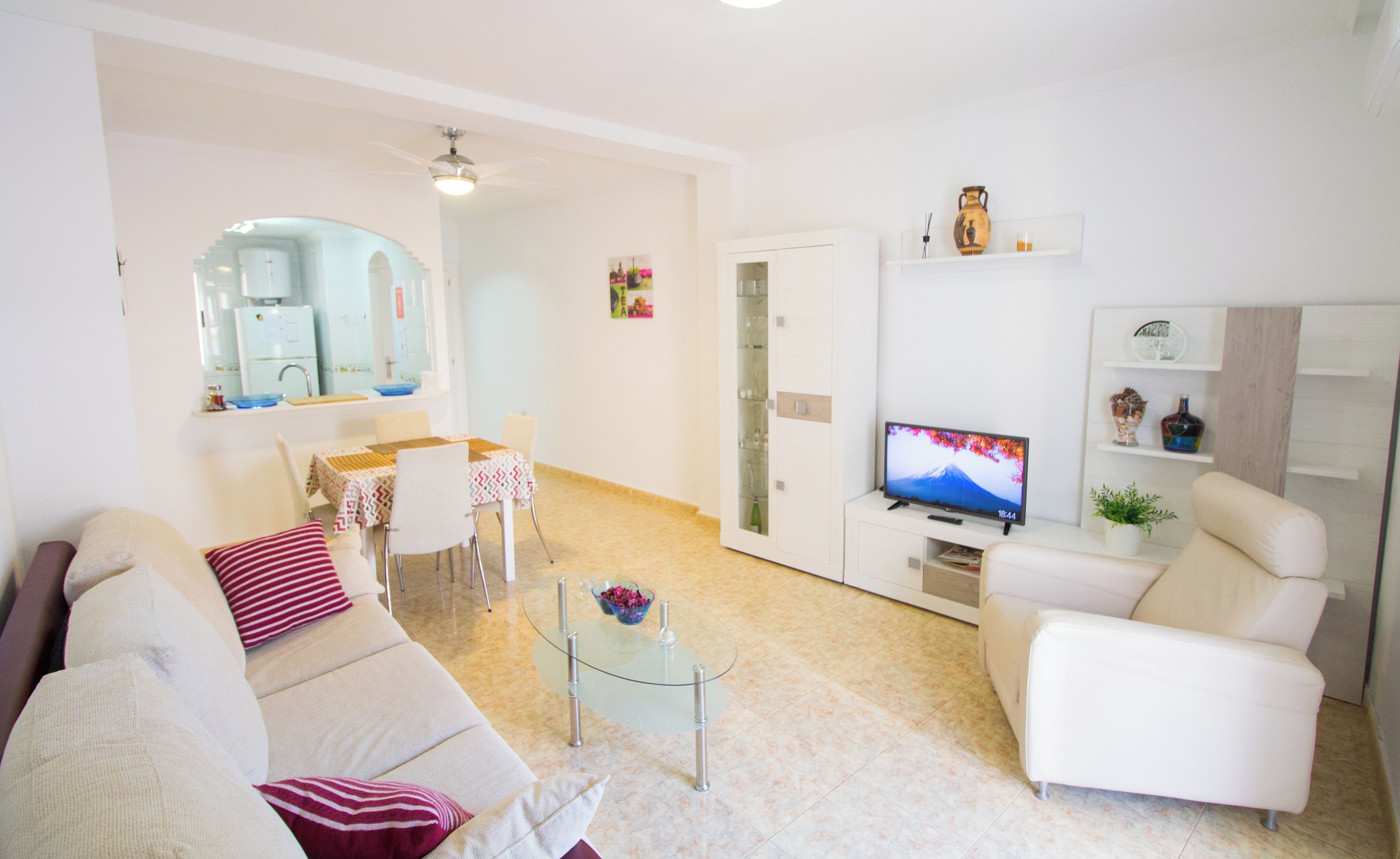 Un soggiorno moderno con un divano, poltrone, un tavolino in vetro, una TV e un'area pranzo con tavolo e sedie.
