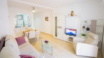 Un soggiorno moderno con un divano, poltrone, un tavolino in vetro, una TV e un'area pranzo con tavolo e sedie.