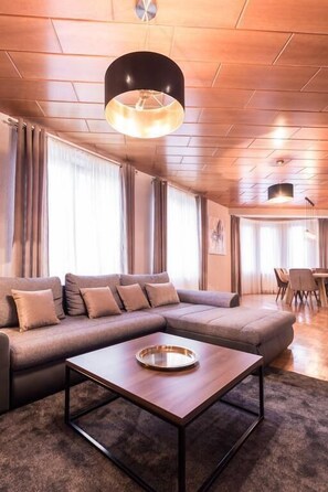 A modern living room with a sectional sofa, a coffee table, and a dining area in the background.