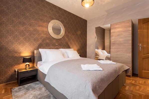 A modern bedroom with a large bed, a bedside table with a lamp, a round mirror on the wall, and a wardrobe.