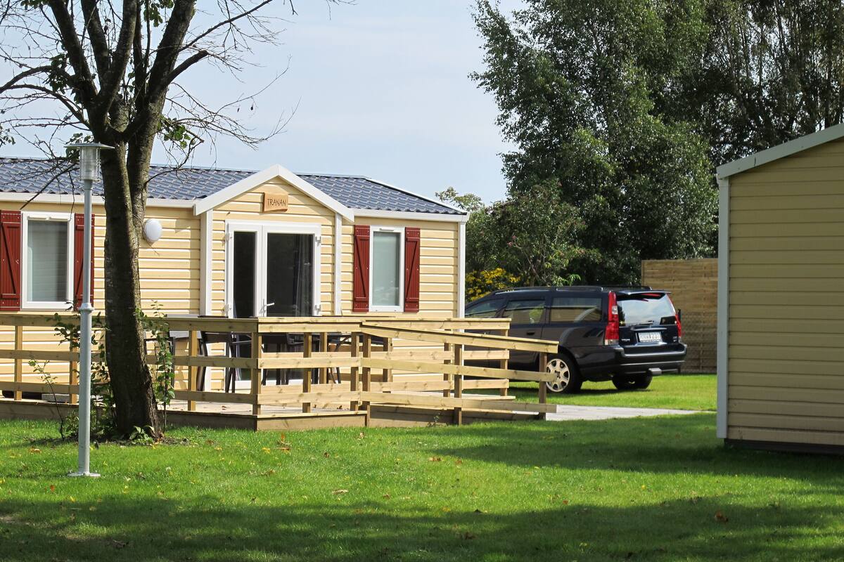 Une maison mobile avec un porche à l’avant et une voiture garée dans l’allée.