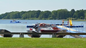 Un muelle a orillas del lago con barcos, un espacio cubierto de césped y un bosque al fondo.