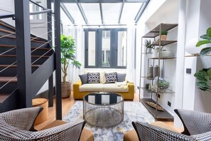 A modern living room with a staircase, a yellow sofa, a coffee table, and a shelving unit with plants. - My Véranda - Le Marais - République- Luxury family suite avec climatisation (Paris)