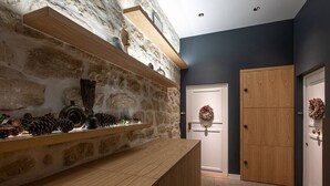 Un pasillo con pared de piedra, estantes de madera con adornos, una puerta con un adorno de ramas y un armario de madera.