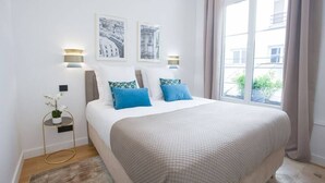 Un dormitorio ordenado con una cama grande, dos lámparas fijadas a la pared y dos cuadros enmarcados.