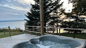 Ein Whirlpool mit einer Holzterrasse und Geländer, mit Blick auf ein Gewässer und Bäume.