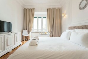 A hotel room with a large bed, a television on a cabinet, a chair, and a window with curtains. - 6 Clouds (Lisbon)