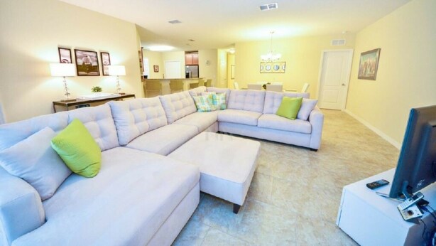 A living room with a large L-shaped sectional sofa, a flat-screen TV, and a small table. - Private Pool - Cozy Vacation Home  Near Disney! (Davenport)