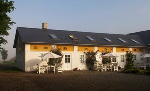 A building with a sloped roof, multiple windows, and outdoor seating with umbrellas. - Nymarksminde Apartments & Farmpark (Vodskov)