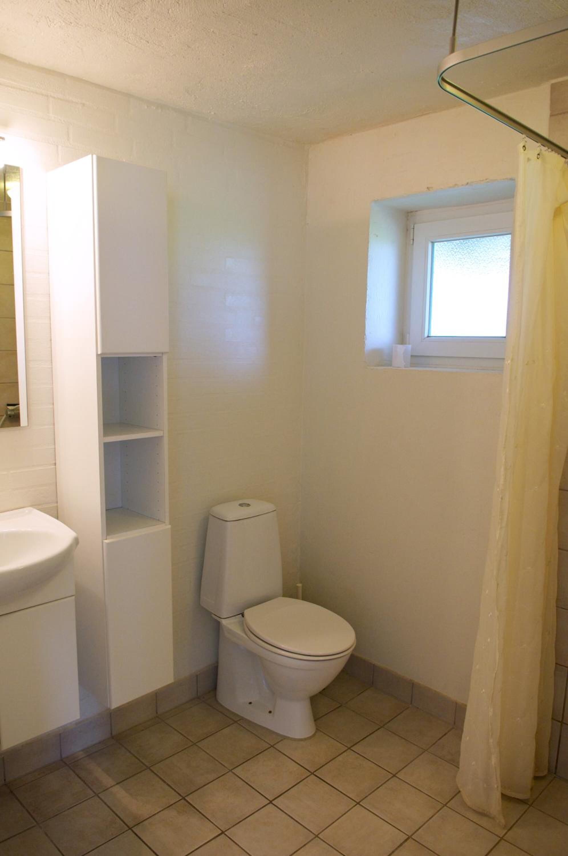 Un baño pequeño y limpio con inodoro, lavamanos y ventana sobre el inodoro.