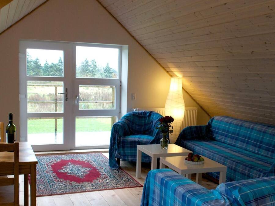 Un dormitorio estilo loft acogedor con un ventanal grande, un sofá escocés, una mesita y una silla.